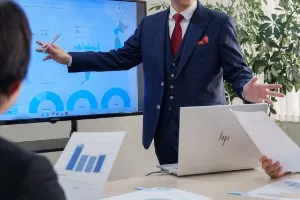 男性社員がモニターに写したデータを指しながらクライアントに説明している様子